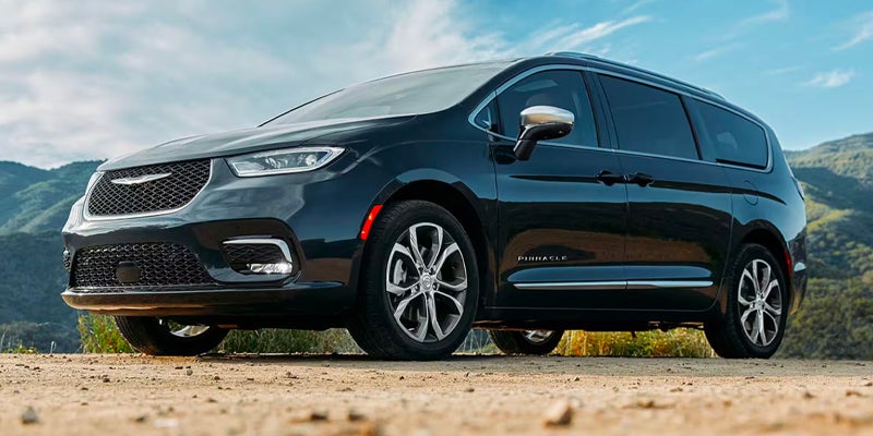 Black Chrysler Pacifica minivan parked on a dirt road with mountains and blue sky in the background