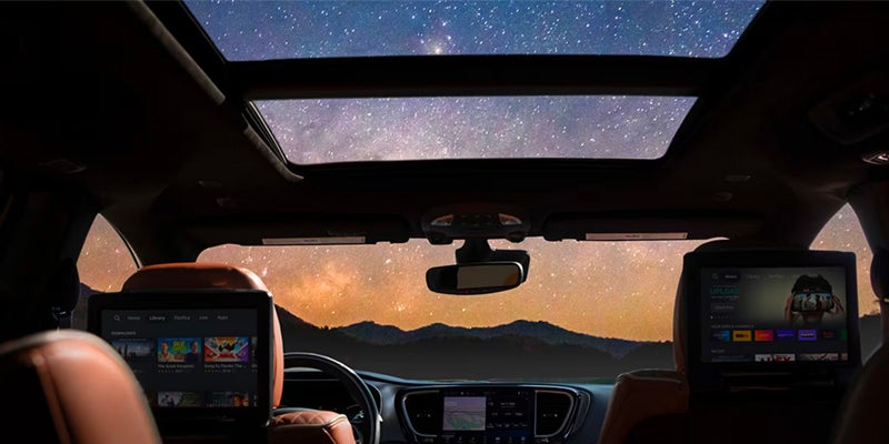 Interior view of a Chrysler Pacifica with a panoramic sunroof showing a star-filled night sky above the cabin.