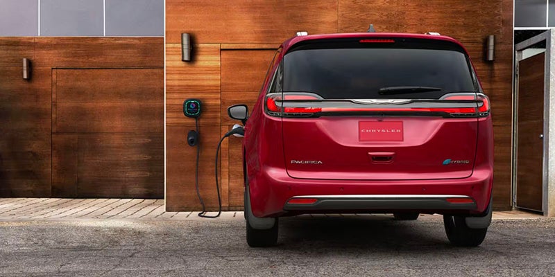 Red Chrysler Pacifica minivan viewed from the rear while connected to an electric vehicle charging station outside a residential garage