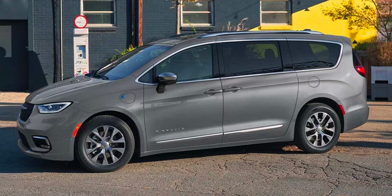 Silver Chrysler Pacifica Hybrid minivan parked on a city street, shown in side profile highlighting the plug-in hybrid design.