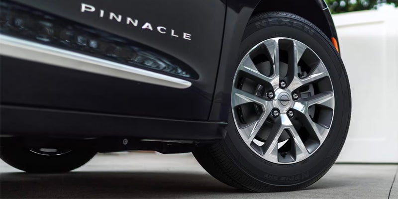 Close-up of a Chrysler Pacifica Pinnacle alloy wheel and lower body trim, showcasing premium exterior styling details.