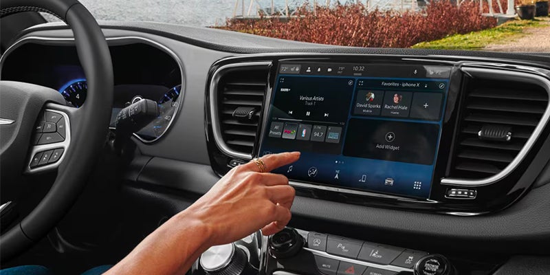 Driver interacting with the Chrysler touchscreen infotainment system displaying media and vehicle controls on a large central display