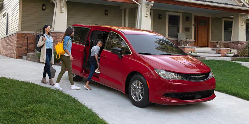 Red Chrysler minivan parked in a residential driveway while passengers enter the vehicle through the sliding side door