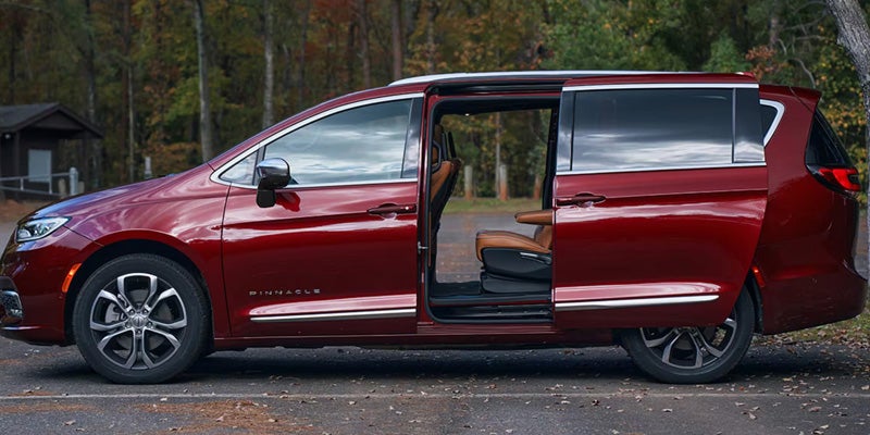 Red Chrysler Pacifica minivan parked outdoors with the passenger-side sliding door open, revealing access to the interior cabin.