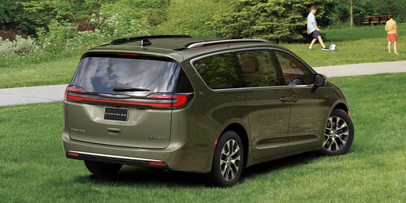 Green Chrysler Pacifica minivan parked on a grassy area, shown from a rear three-quarter angle with a park-like setting in the background
