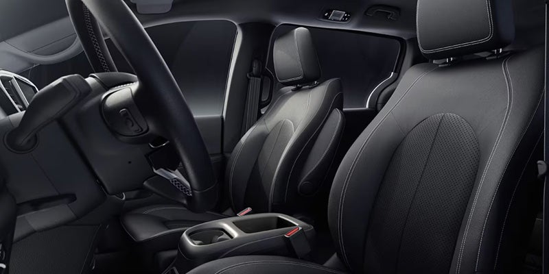 Front cabin view of a Chrysler Pacifica showing black leather seats, center console, steering wheel, and dashboard controls.