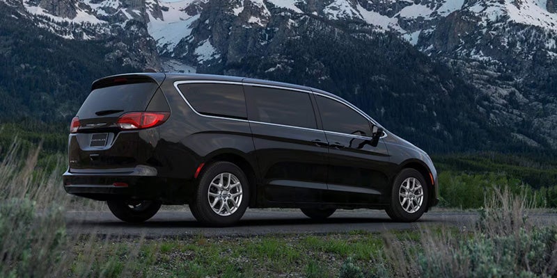 Black Chrysler minivan parked outdoors with snow-capped mountains and grassy terrain in the background