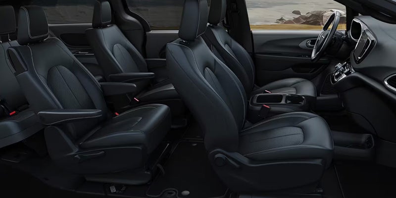 Interior view of a Chrysler minivan showing black leather front and second-row seats with spacious passenger accommodations.