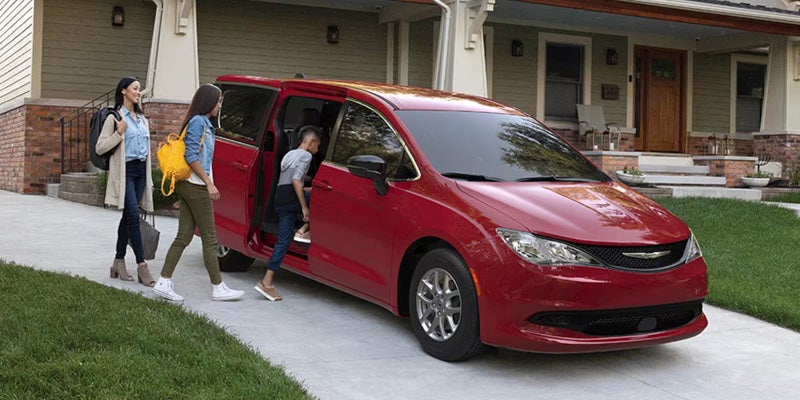 Red Chrysler minivan parked in a residential driveway while passengers enter the vehicle near a suburban home