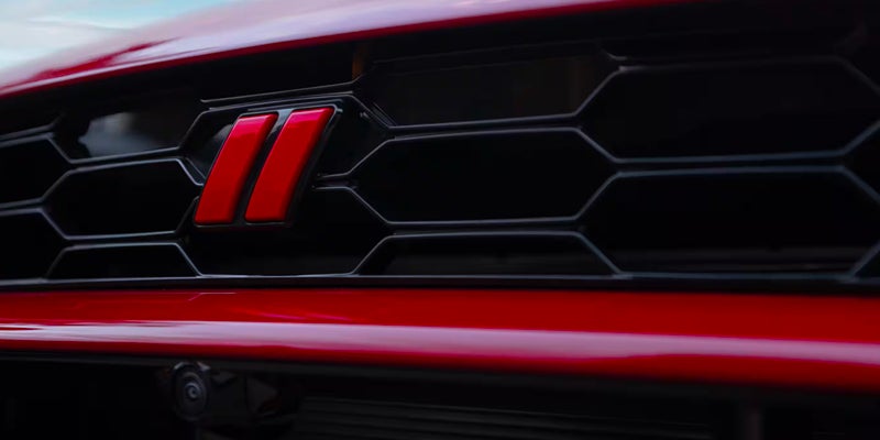 Close-up of the Dodge Hornet front grille featuring the red Dodge slash emblem on a black honeycomb mesh design.
