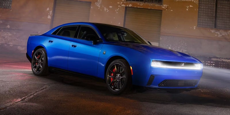 Blue Dodge Charger Daytona parked on a wet urban street at night, shown from a front three-quarter
