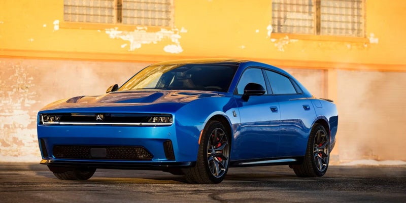 Blue Dodge Charger Daytona performance sedan driving on a paved surface, showcasing its sporty profile and black wheels.
