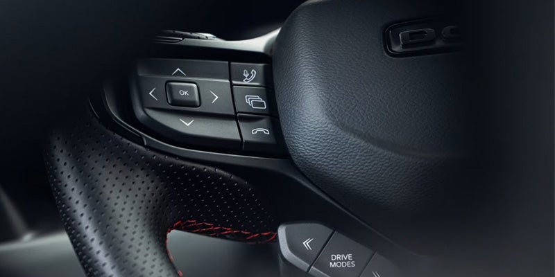 Close-up of the Dodge Charger Daytona steering wheel showing integrated control buttons and red contrast stitching.
