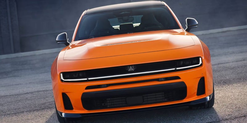 Front view of an orange Dodge Charger Daytona featuring a wide grille, slim LED headlights, and a muscular stance.
