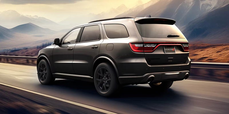 Black Dodge Durango SUV driving on an open highway with mountains and a scenic landscape in the background.