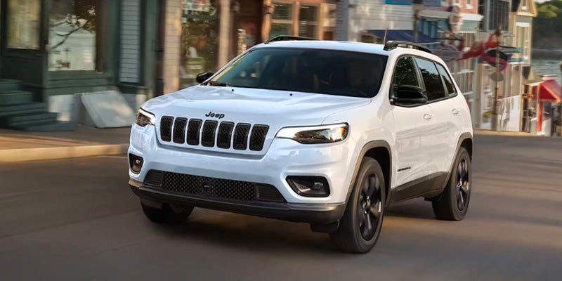 White Jeep Cherokee SUV driving through a city street, viewed from a front three-quarter angle