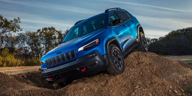 Blue Jeep Cherokee Trailhawk climbing a dirt mound, showcasing its off-road suspension and rugged design.