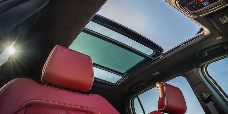 Interior view of a car with two open sunroofs and two red leather bucket seats, bathed in sunlight.