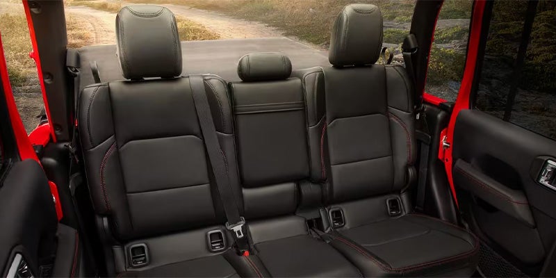Back view of a car's black leather interior with three passenger seats and red contrast stitching.