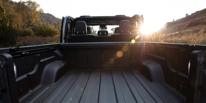 View from inside an empty pickup truck bed looking towards the seats, with a sunset and mountains in the background.
