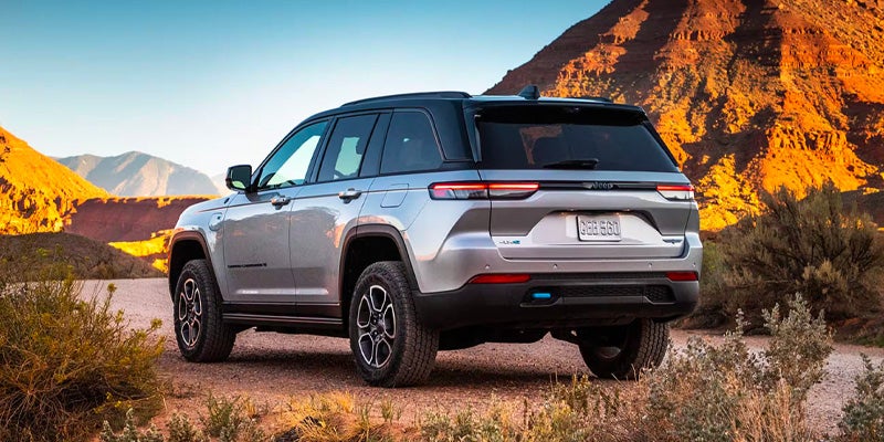 Rear view of a silver 2022 Jeep Grand Cherokee 4xe with black roof, parked on a dirt road in a desert.