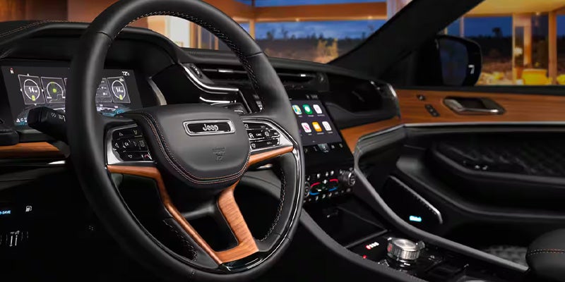 Close-up of a luxurious car interior with a black leather and wood-grain steering wheel, digital dashboard and touchscreen.