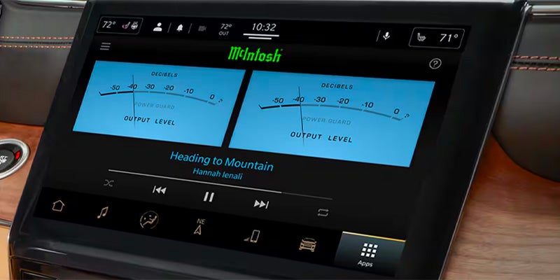 A car's digital dashboard display shows music playback with a McIntosh logo and analog-style output meters.