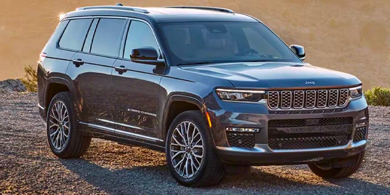 A dark gray Jeep Grand Cherokee L SUV, viewed from the front quarter, parked on a gravel surface outdoors.