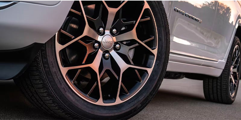 Close-up of a Jeep Grand Cherokee’s front wheel, with bronze and black alloy rim, and a glimpse of the rear wheel.