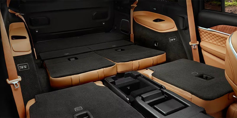 The cargo area of a large vehicle with all rear seats folded flat, covered in black carpet with tan leather trim.