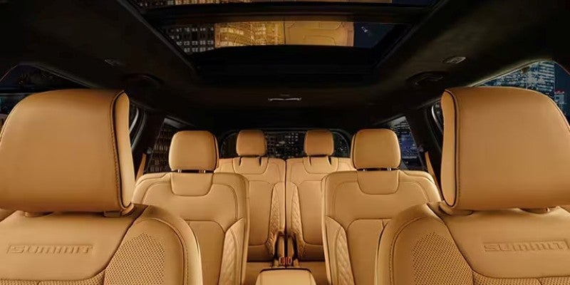 Interior of a car with rows of light brown leather seats, a sunroof, and city lights visible outside.
