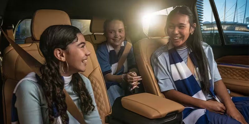 Three smiling teen girls in a car, two in blue and white striped shirts, sunlight streaming from the window.