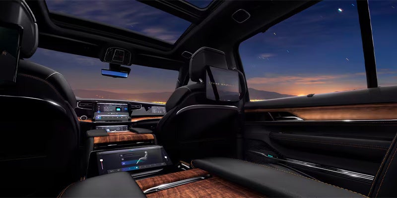 Luxurious car interior at night with large screens, wood accents, and a starry sky visible through the windows and sunroof.