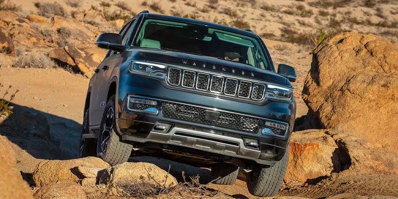 Dark gray Grand Wagoneer SUV driving over large rocks on an off-road desert trail.