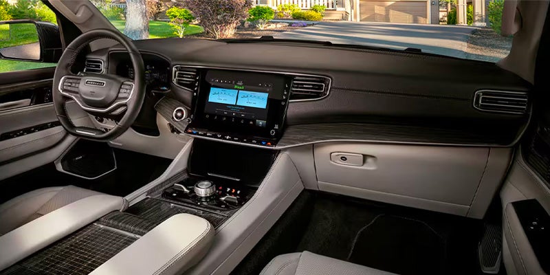 Dark, luxurious car interior with black steering wheel, large infotainment screens, light seats, and wood grain accents.