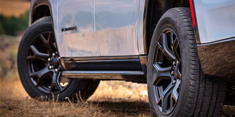 Close-up of a light-colored SUV's side, showing two black wheels with dark rims, black running boards, and a red fender accent.