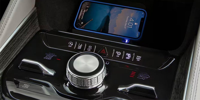 A smartphone charging on a wireless pad above a modern car's glossy control panel with a large silver dial.