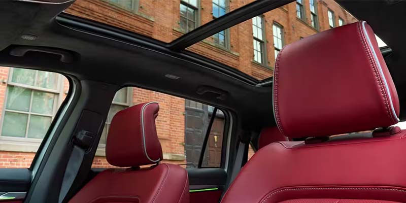 Interior of a car with deep red leather seats, white stitching, a black ceiling, and a panoramic sunroof.