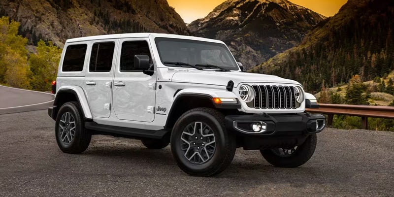 White Jeep Wrangler Unlimited parked on a mountain road with trees and mountains in the background.