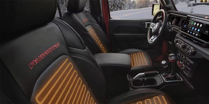 Heated black leather seats with red "RUBICON" embroidery and a modern infotainment system in a car interior.