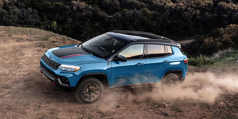 Blue Jeep Compass driving on a dusty off-road trail, viewed from above