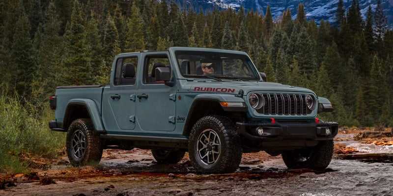 Light blue Jeep Gladiator Rubicon pickup truck parked on a rocky trail surrounded by pine trees