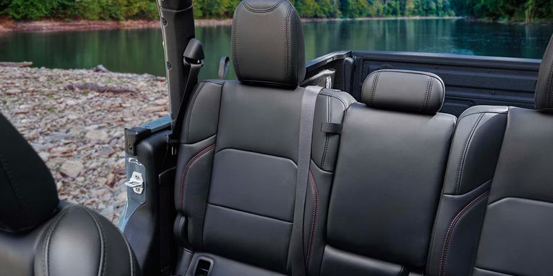 Interior rear seating area of a Jeep Gladiator with black leather seats and open-air cabin configuration beside a lakeside setting.