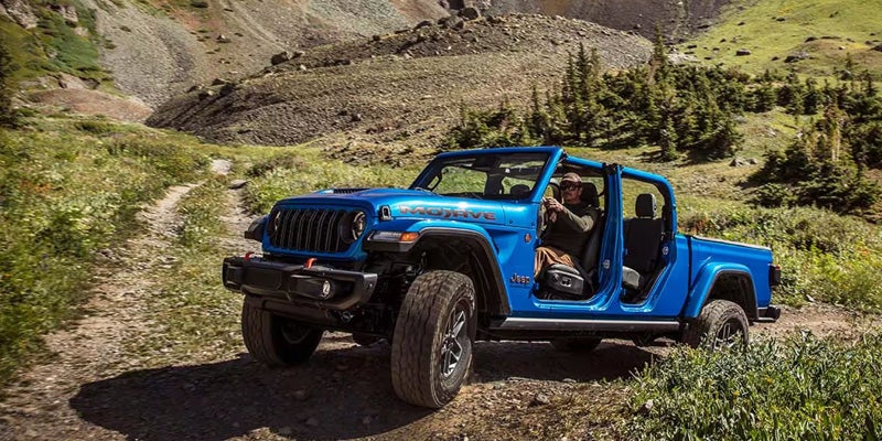 Blue Jeep Gladiator with removable doors parked on a mountain trail, highlighting its open-air design and off-road features.