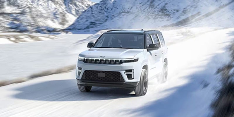 White Jeep Wagoneer driving through a snow-covered landscape, showcasing all-weather performance and LED lighting