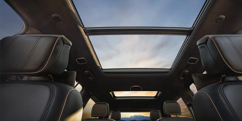Interior view of a car with a large panoramic sunroof and smaller rear sunroof, showing the sky and clouds.