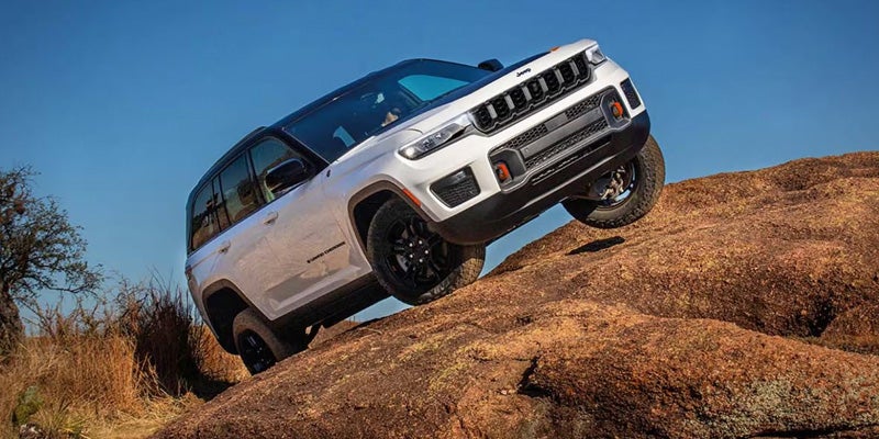 White Jeep Grand Wagoneer climbing a rocky slope, demonstrating off-road capability in a rugged landscape.