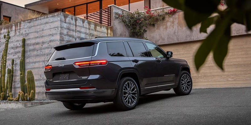 Black Jeep Grand Wagoneer parked in front of a modern home, showcasing its rear design, LED taillights, and premium SUV styling