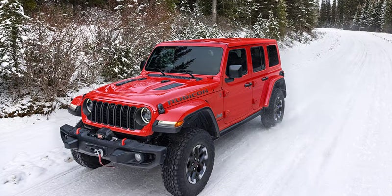 Red Jeep Wrangler Rubicon driving on a snow-covered road through a forested landscape