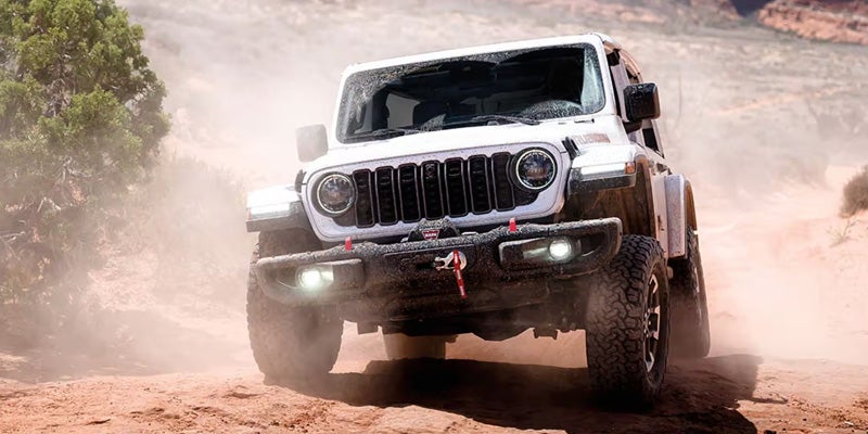 White Jeep Wrangler Rubicon driving through a dusty off-road trail, showcasing its rugged tires